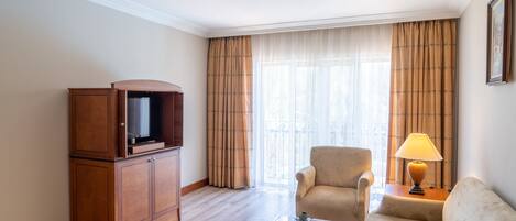 Una habitación de hotel con un armario de madera, un televisor, un sofá, una mesa de centro con fruta y una lámpara.