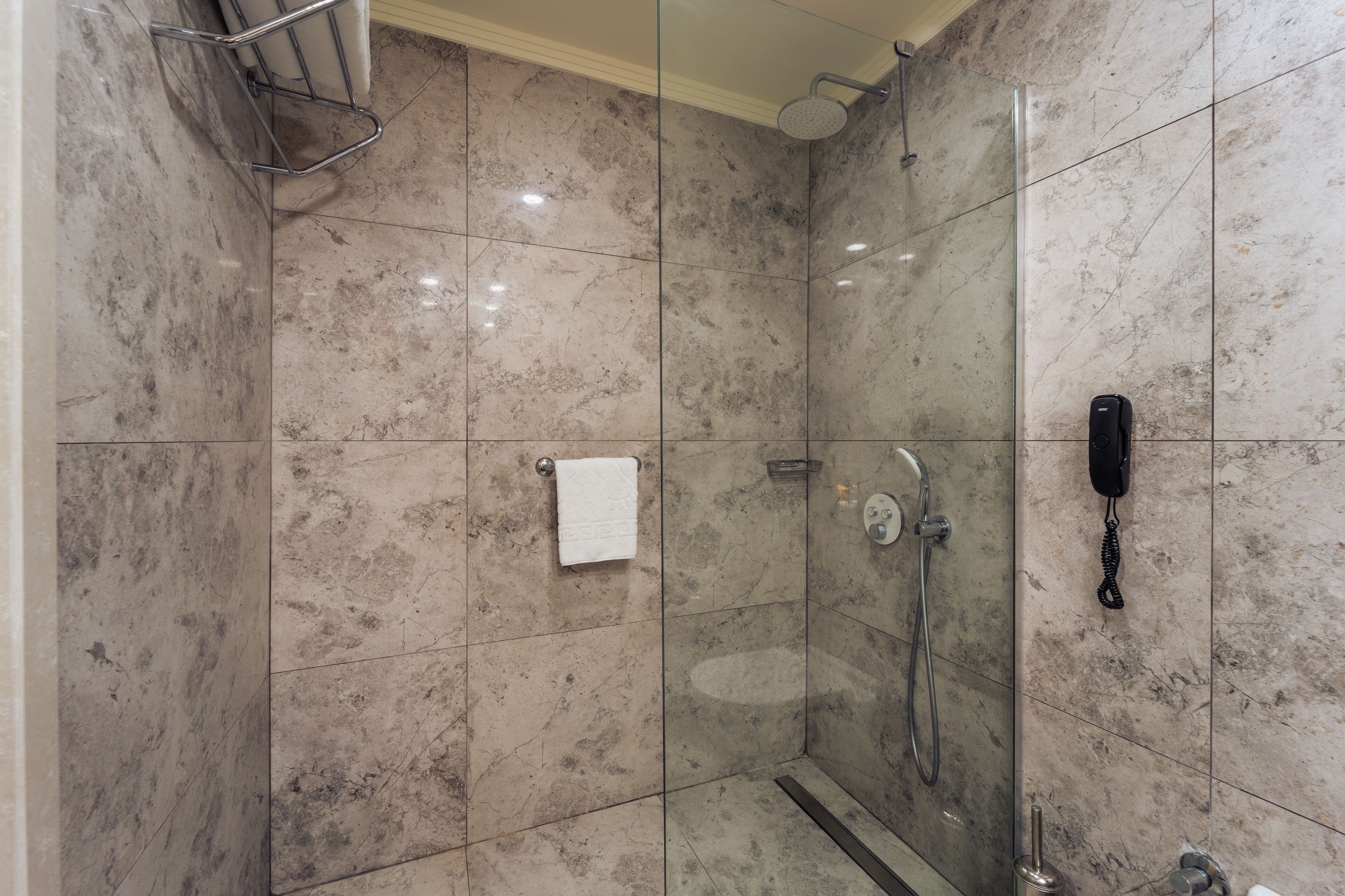 Un baño moderno con cabina de ducha de vidrio, un perchero y un teléfono fijo en la pared.