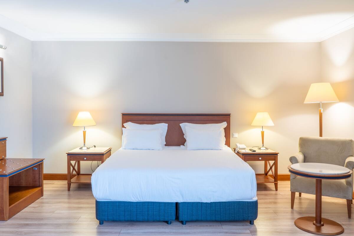 A hotel room with a large bed, two bedside tables with lamps, a chair, and a small table.