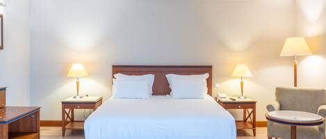 Una habitación de hotel con una cama grande, dos mesitas de noche con lámparas, una silla y una pequeña mesa.