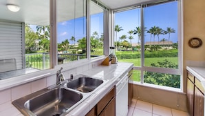 A kitchen with a large window, a stainless steel sink, and a knife block on the counter. - Oceanfront Realty - The Cliffs at Princeville (Princeville)