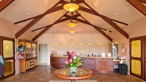 A reception area with a wooden reception desk, a vase with flowers, and a stone-tiled floor. - Oceanfront Realty - The Cliffs at Princeville (Princeville)