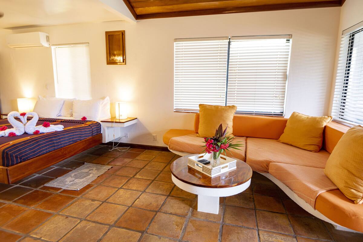 Une chambre d’hôtel avec un lit, un canapé, une table basse et une fenêtre avec des stores.