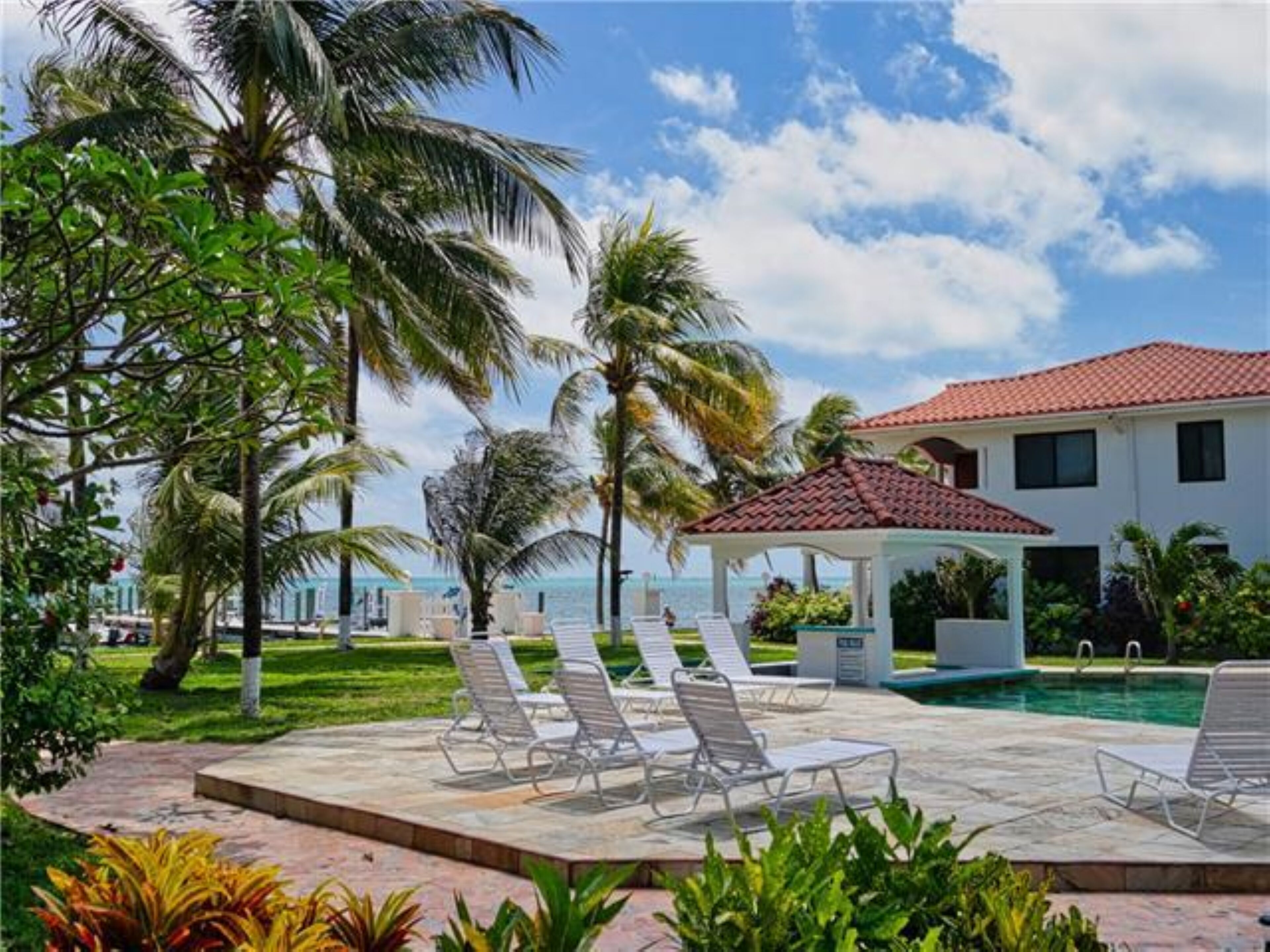 A pool area with lounge chairs, a gazebo, and a house with a red-tiled roof.