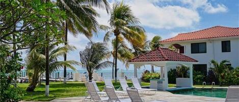 A pool area with lounge chairs, a gazebo, and a house with a red-tiled roof.