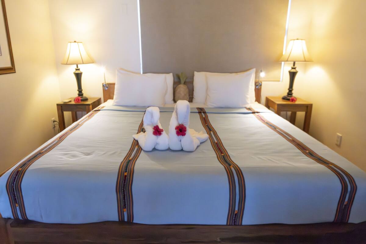 Un lit bien fait, avec du linge de lit blanc et des coussins décoratifs en forme de cygne, flanqué de deux lampes de chevet.