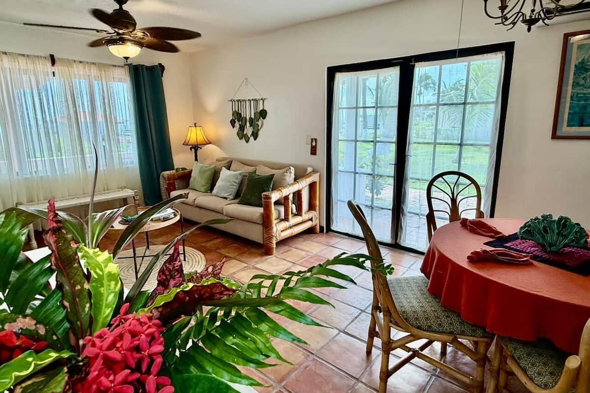 Un salon comprenant un canapé, une table à manger avec des chaises, un ventilateur de plafond et une grande fenêtre donnant sur un paysage verdoyant.