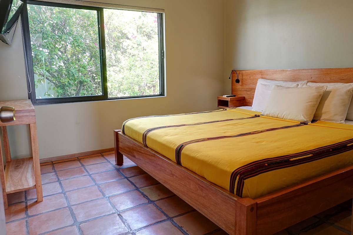 Une chambre à coucher avec un lit en bois, une table de chevet, une commode et une fenêtre donnant sur des arbres.