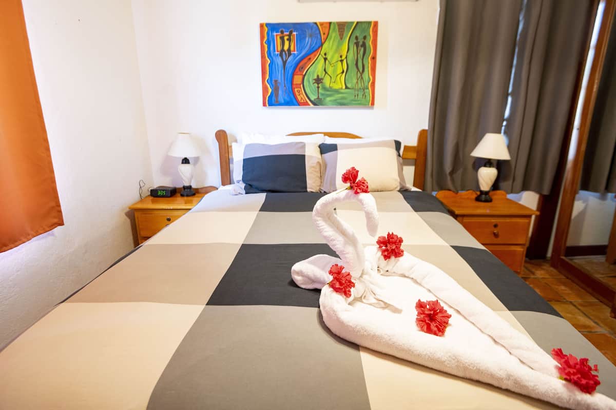 Une chambre d’hôtel avec une couvre-lit à carreaux, un tableau au mur et une table de chevet avec une lampe.