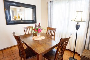 Una mesa de comedor con cuatro sillas, un jarrón con flores, un espejo en la pared y una lámpara de pie.