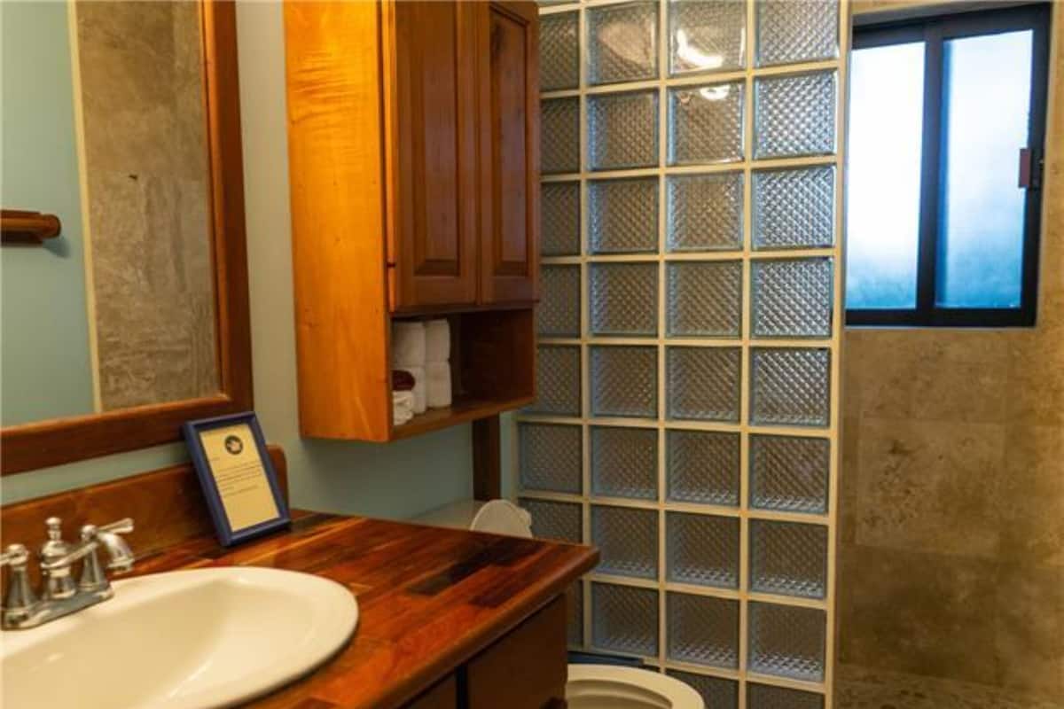 Une salle de bain avec un meuble-lavabo en bois, un lavabo blanc, des toilettes et un espace douche doté d’une porte en verre.