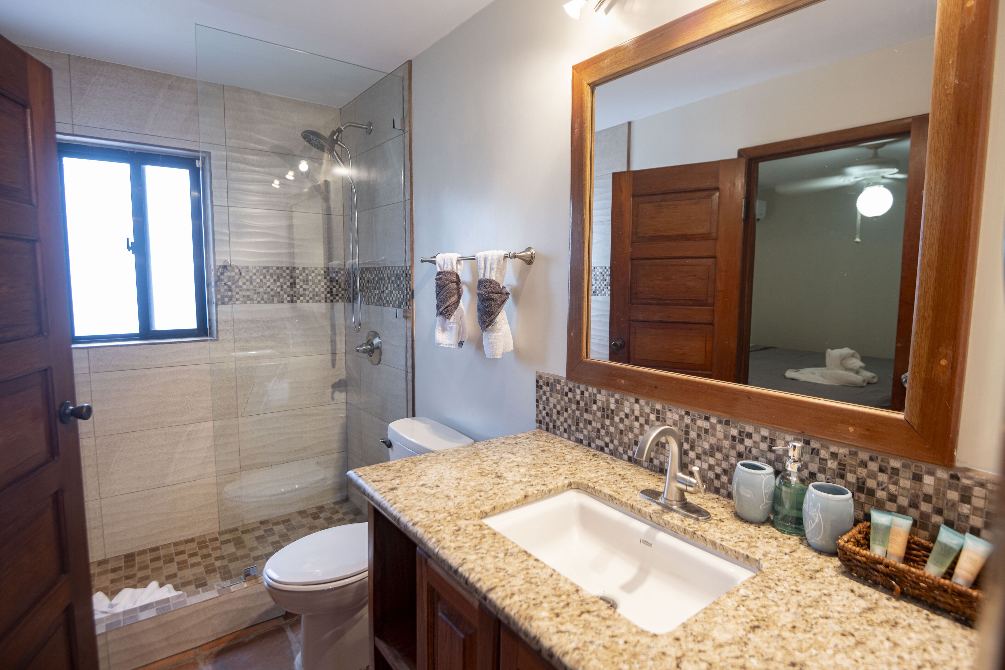 A bathroom with a granite countertop sink, a large mirror, and a shower area.