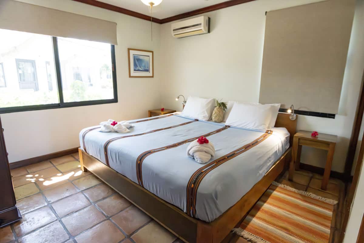 Une chambre d’hôtel avec un grand lit, deux tables de chevet, une commode, une fenêtre et un appareil de climatisation.