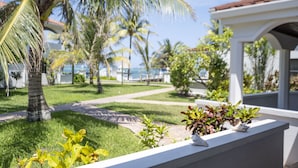 Ein gepflegter Garten mit Palmen und verschiedenen Pflanzen, ein Weg, der zu einem Gebäude mit Ziegeldach führt, und Blick aufs Meer.