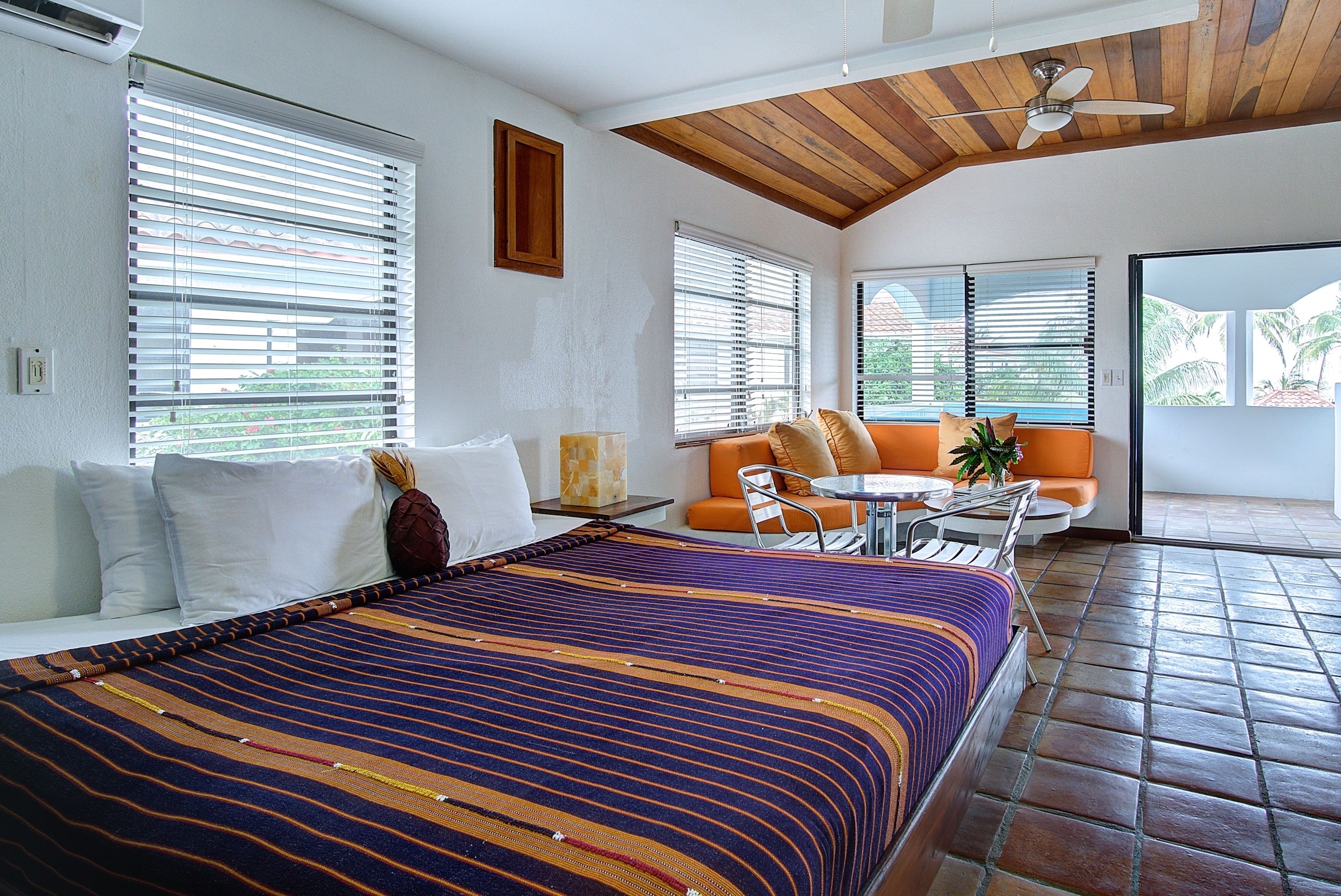 A hotel room with a bed, a sofa, a small table, and a ceiling fan.