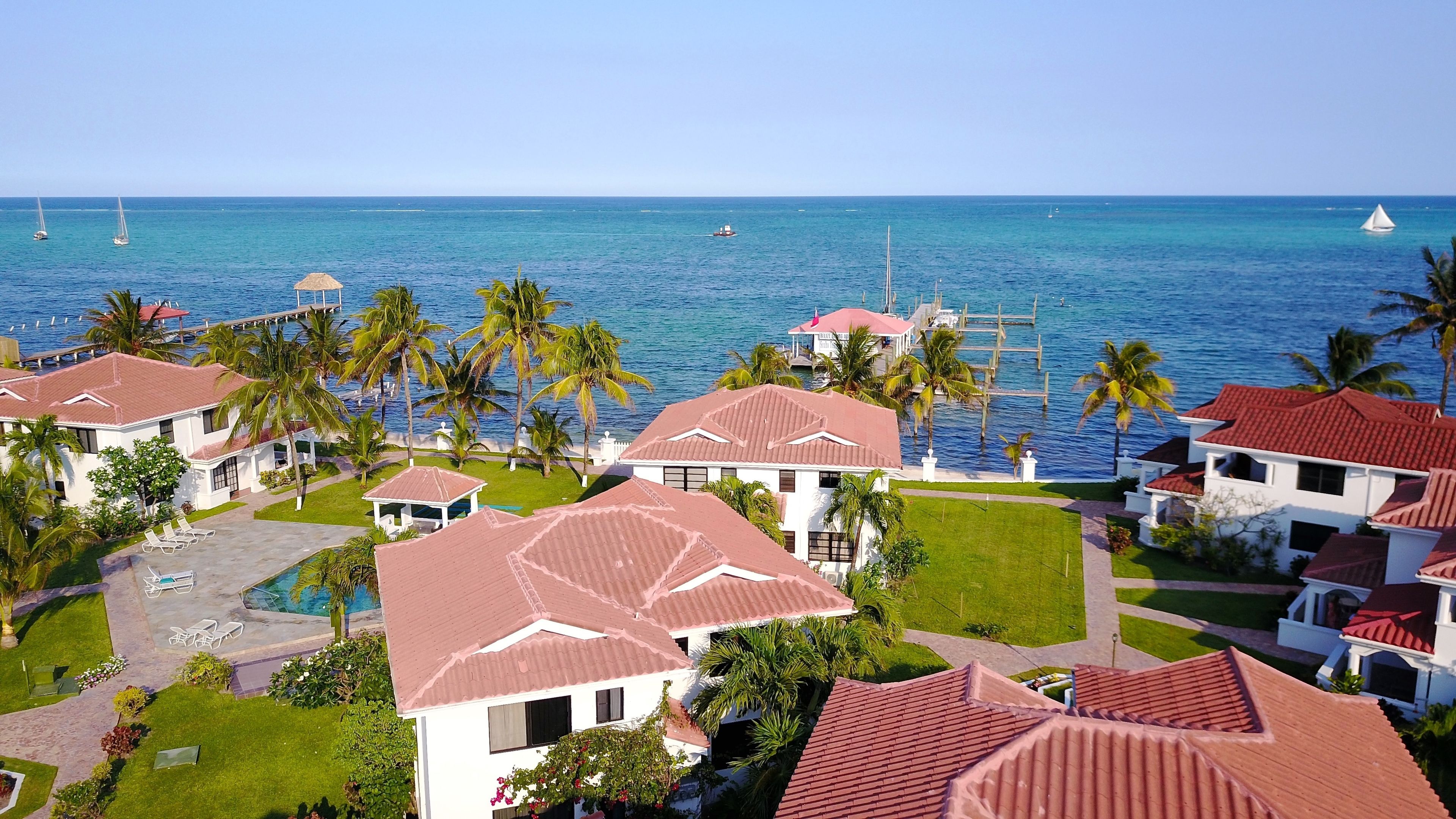 A resort with multiple buildings, a pool, and a view of the ocean with sailboats.