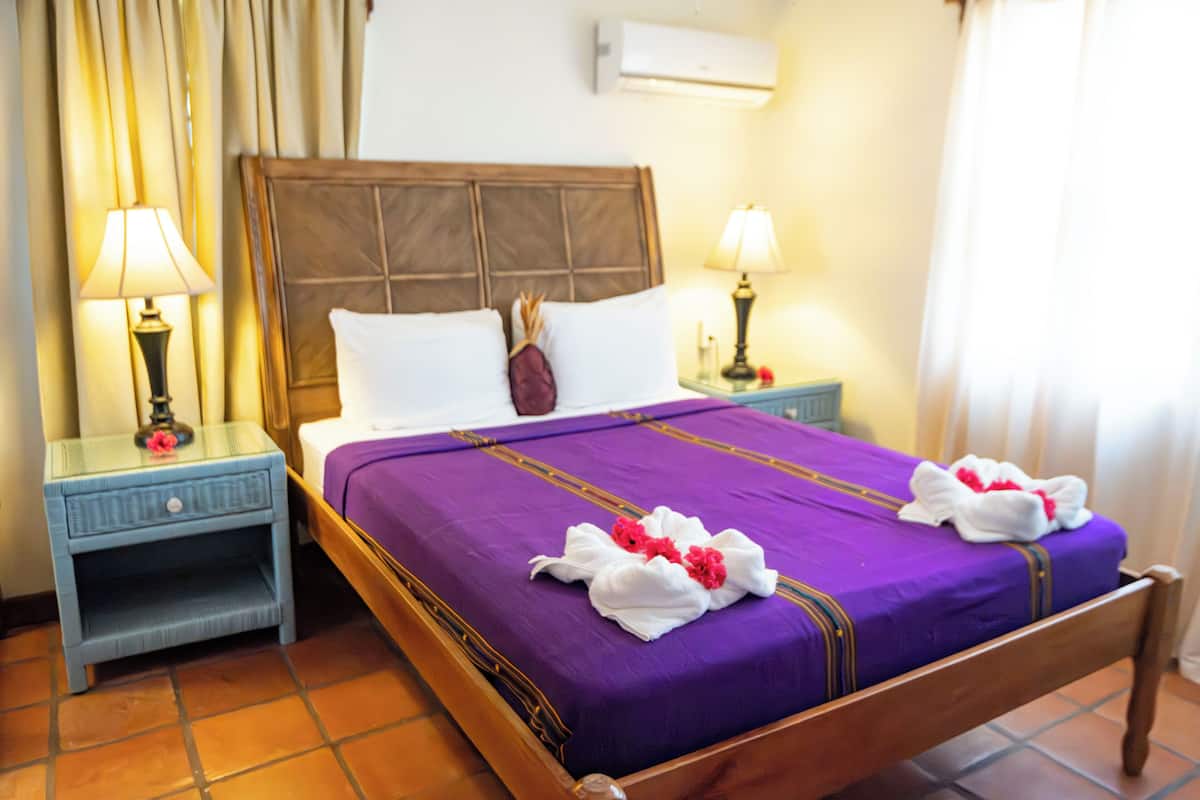 Une chambre d’hôtel avec un lit en bois, une literie violette et deux tables de chevet avec des lampes.