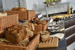 Ein Buffet mit verschiedenen Brotsorten und Gebäck, präsentiert in Weidenkörben und auf einer Holzbrett.