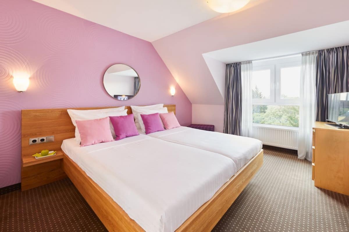 A bedroom with a large bed, two bedside tables, a mirror, and a window with curtains.