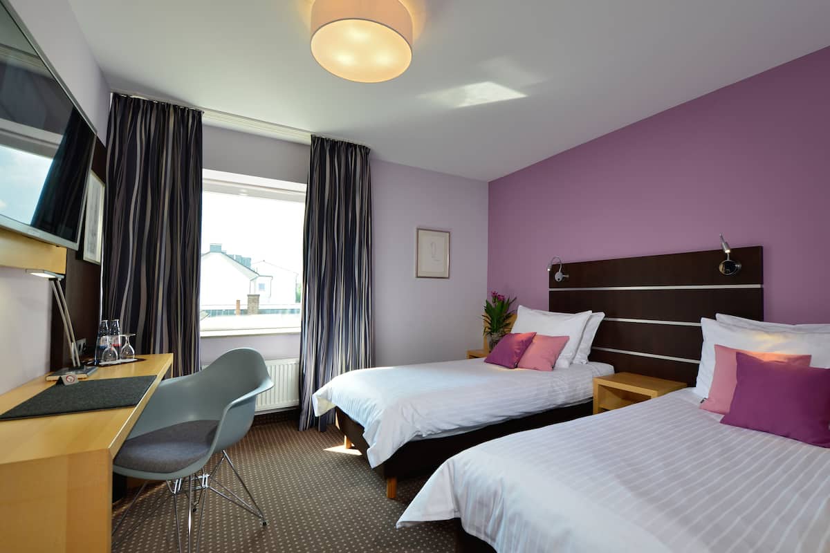 A hotel room with two beds, a desk, a chair, and a TV.