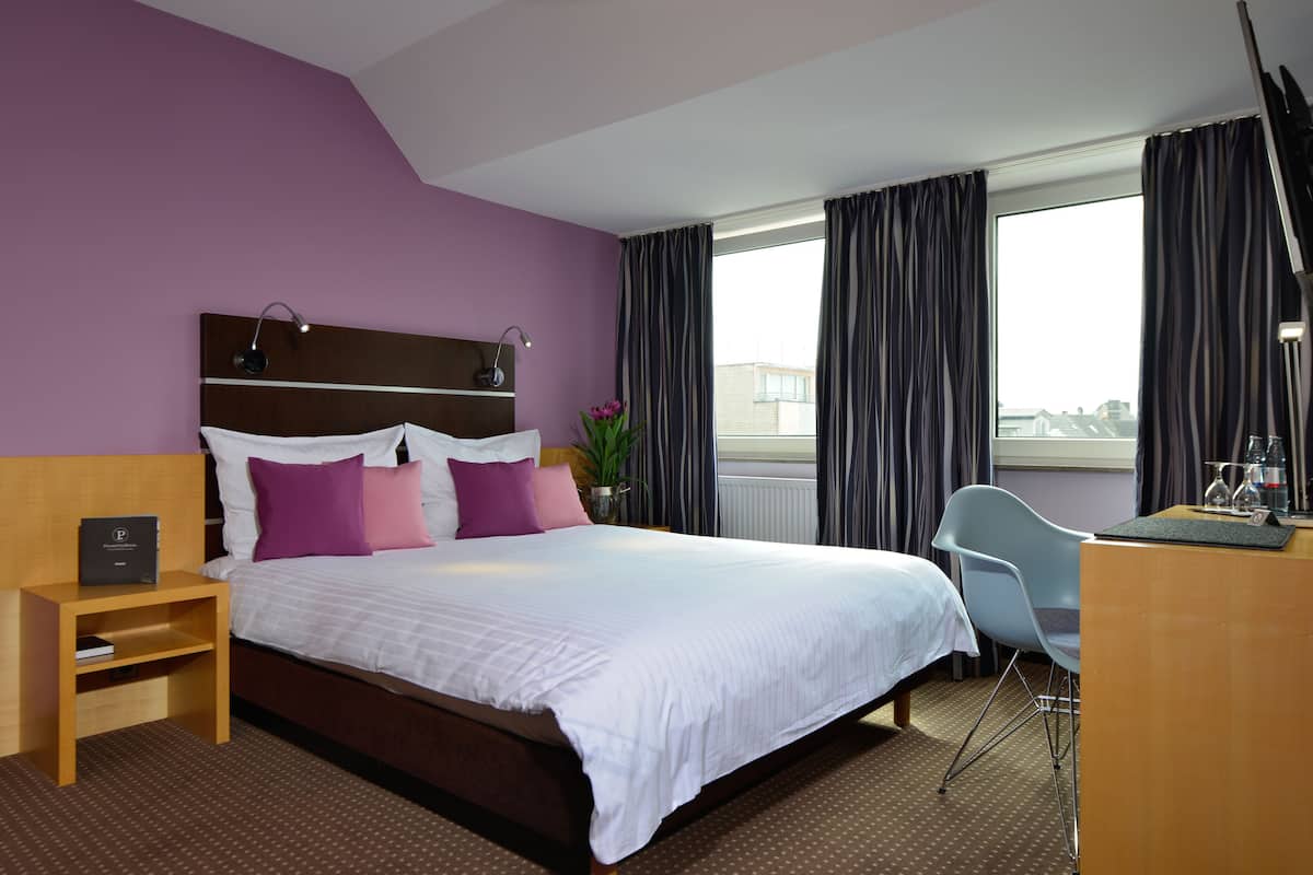 A hotel room with a large bed, a desk, a chair, and a nightstand.