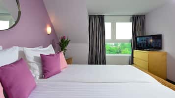 Habitación de hotel con cama, televisión, ventana con cortinas, espejo y planta en maceta.