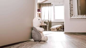 A plush toy sitting on a wooden floor in a room with a window, a lamp, and a radiator.