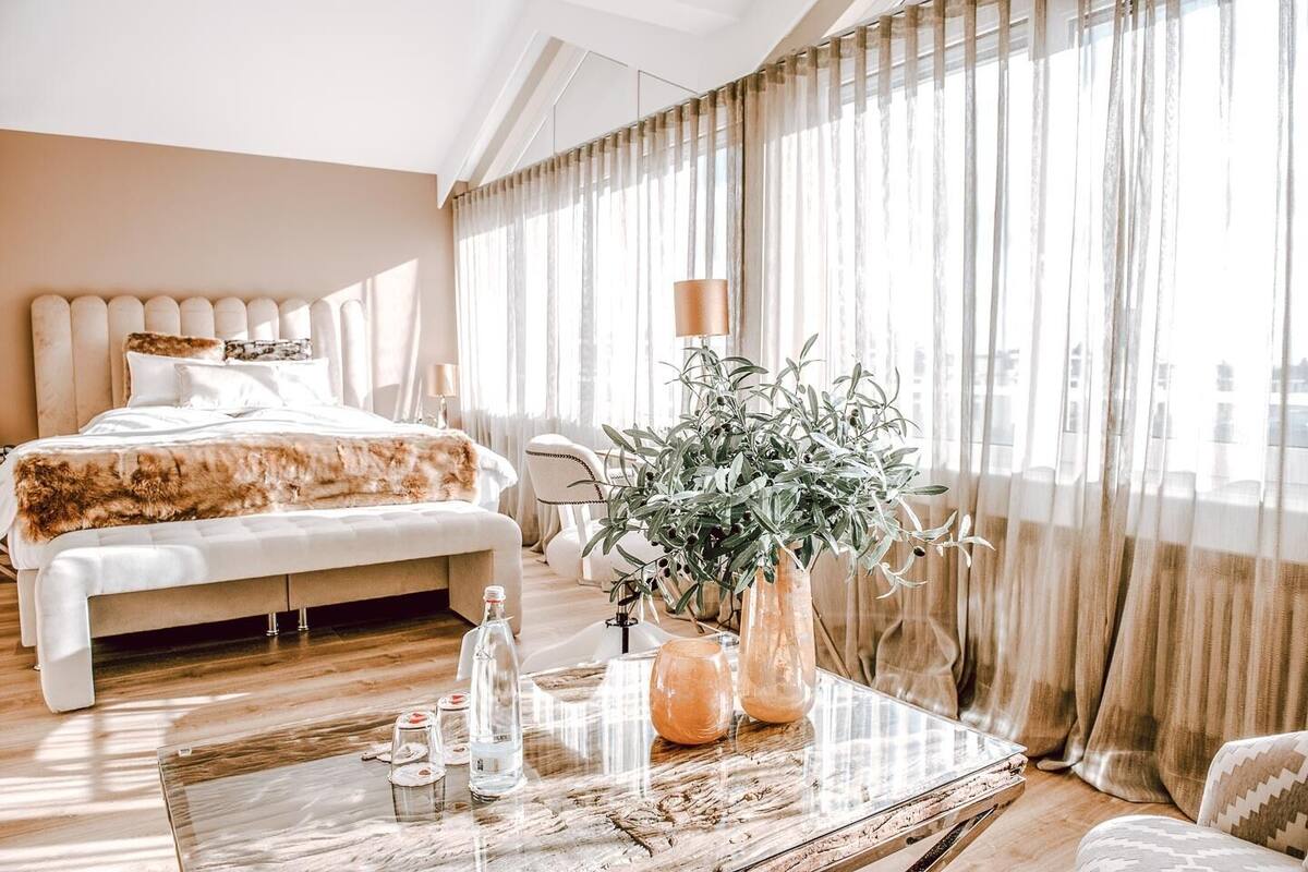 A modern hotel room with a large bed, a wooden coffee table, and a potted plant.