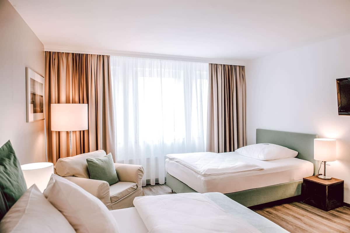 A hotel room with two beds, a sofa, a lamp, and a large window with curtains.