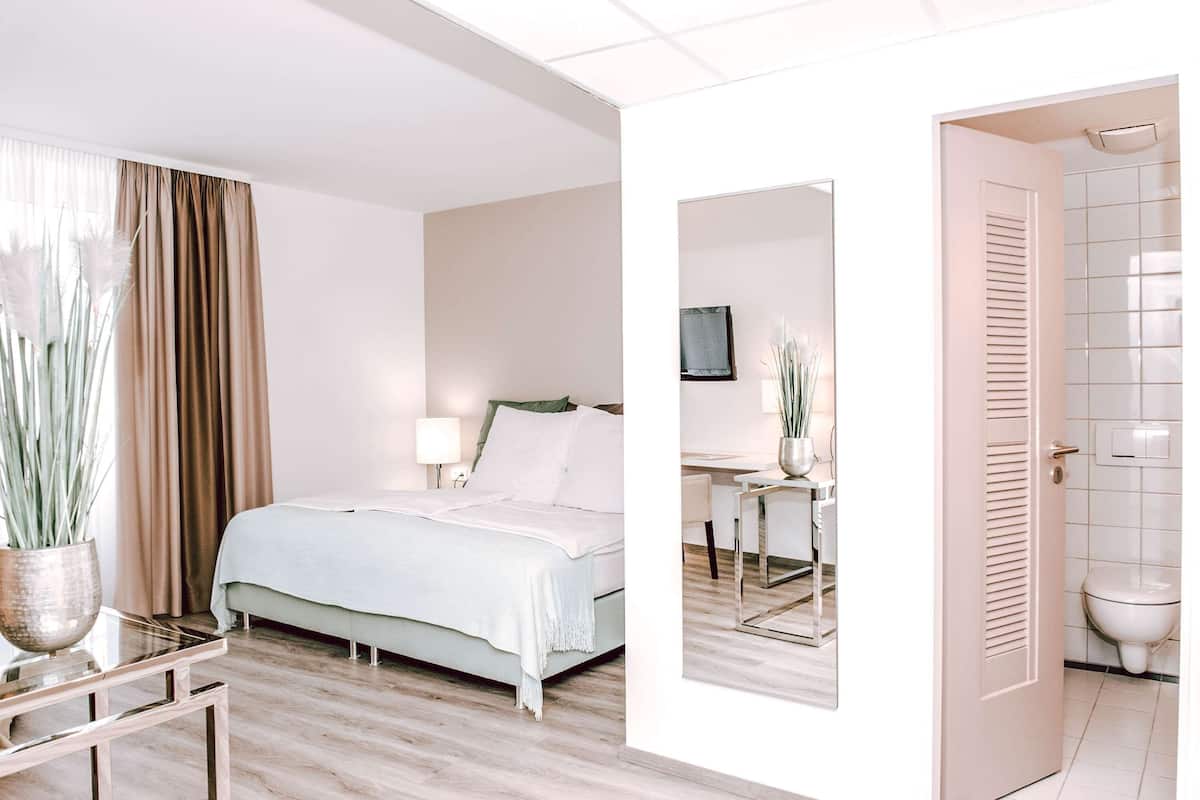 A hotel room with a bed, bedside table, and a mirror reflecting the bathroom.