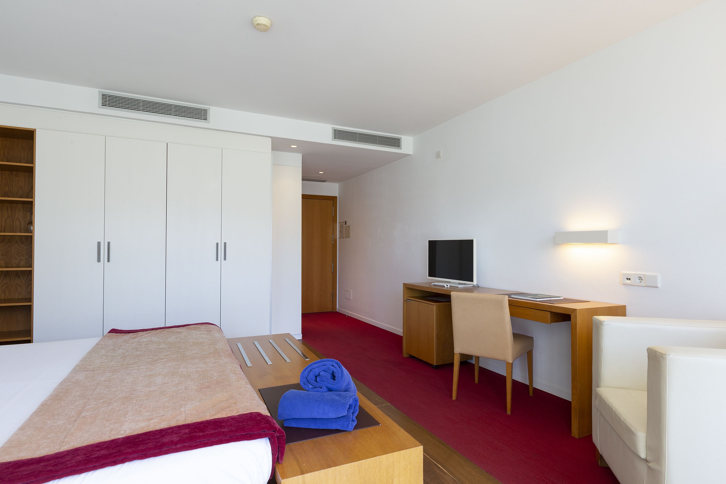 A hotel room with a bed, a desk, a chair, a TV, and a wardrobe.