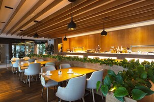 A modern cafe with wooden ceiling beams, pendant lighting, and a long counter with a variety of food items.