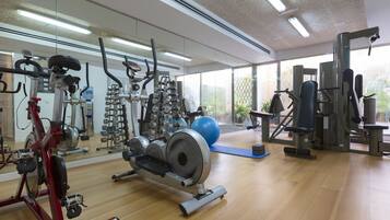 Un gimnasio con máquinas de cardio, equipo de levantamiento de pesas y un espejo grande.