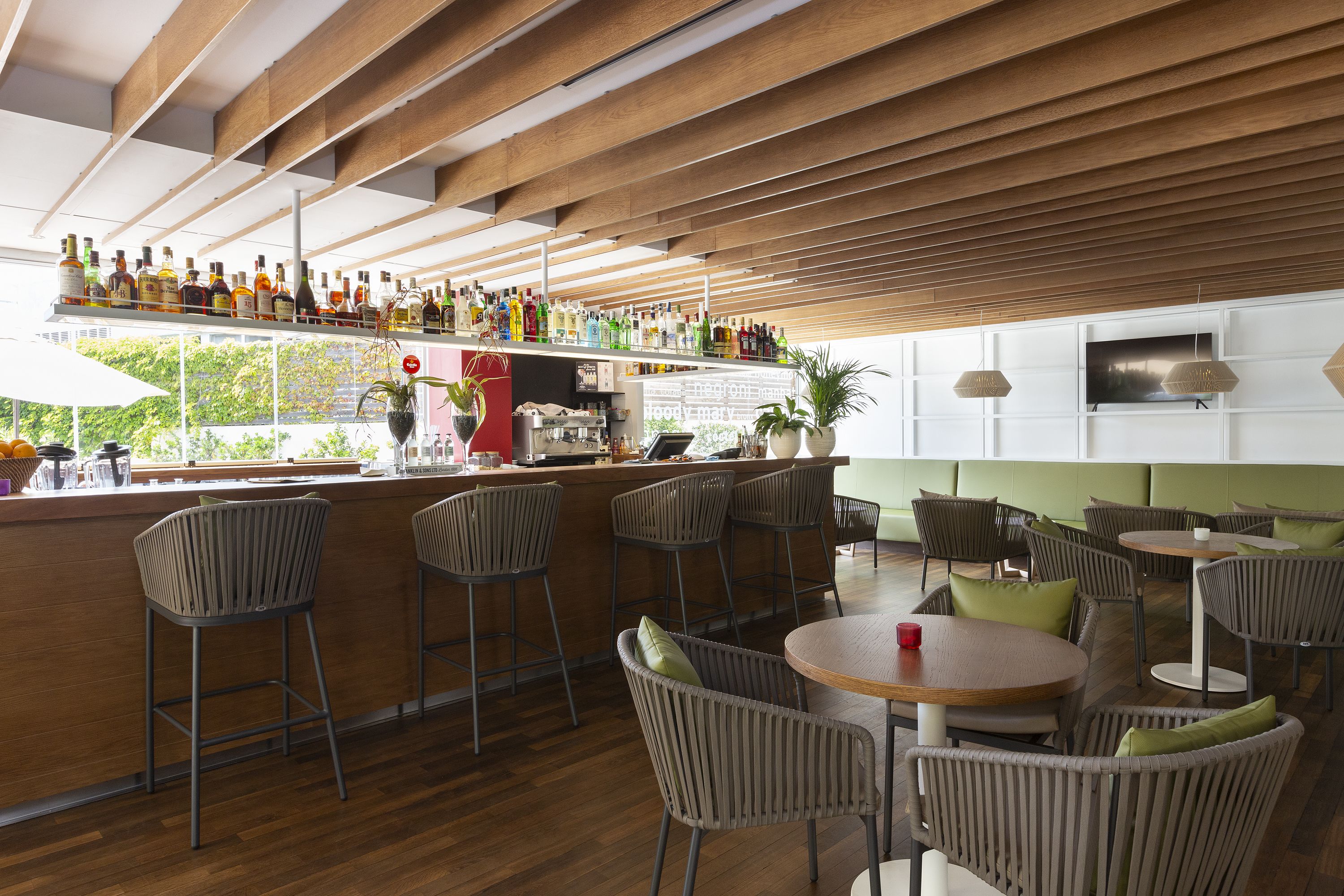 A bar area with wooden ceiling, bar stools, and a variety of bottles. There are tables and chairs for seating.