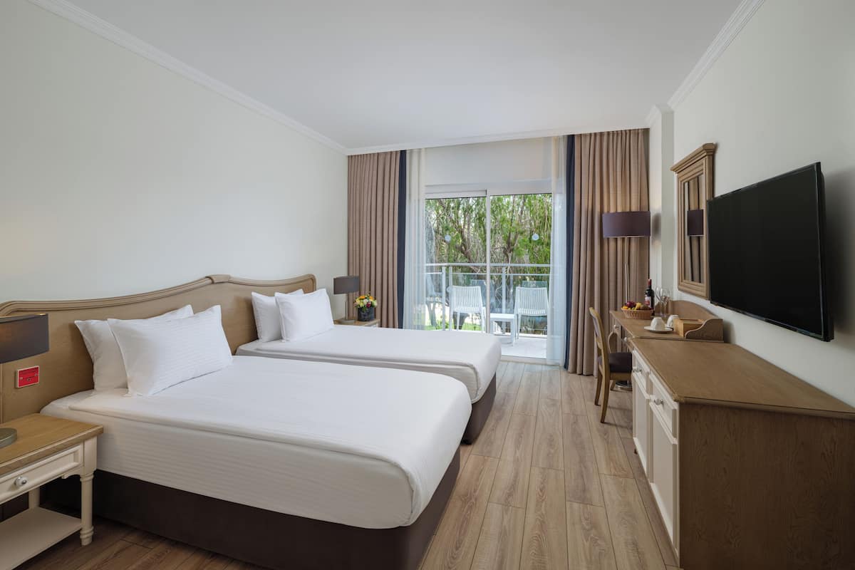 A hotel room with two beds, a TV, a desk, and a balcony with a view.