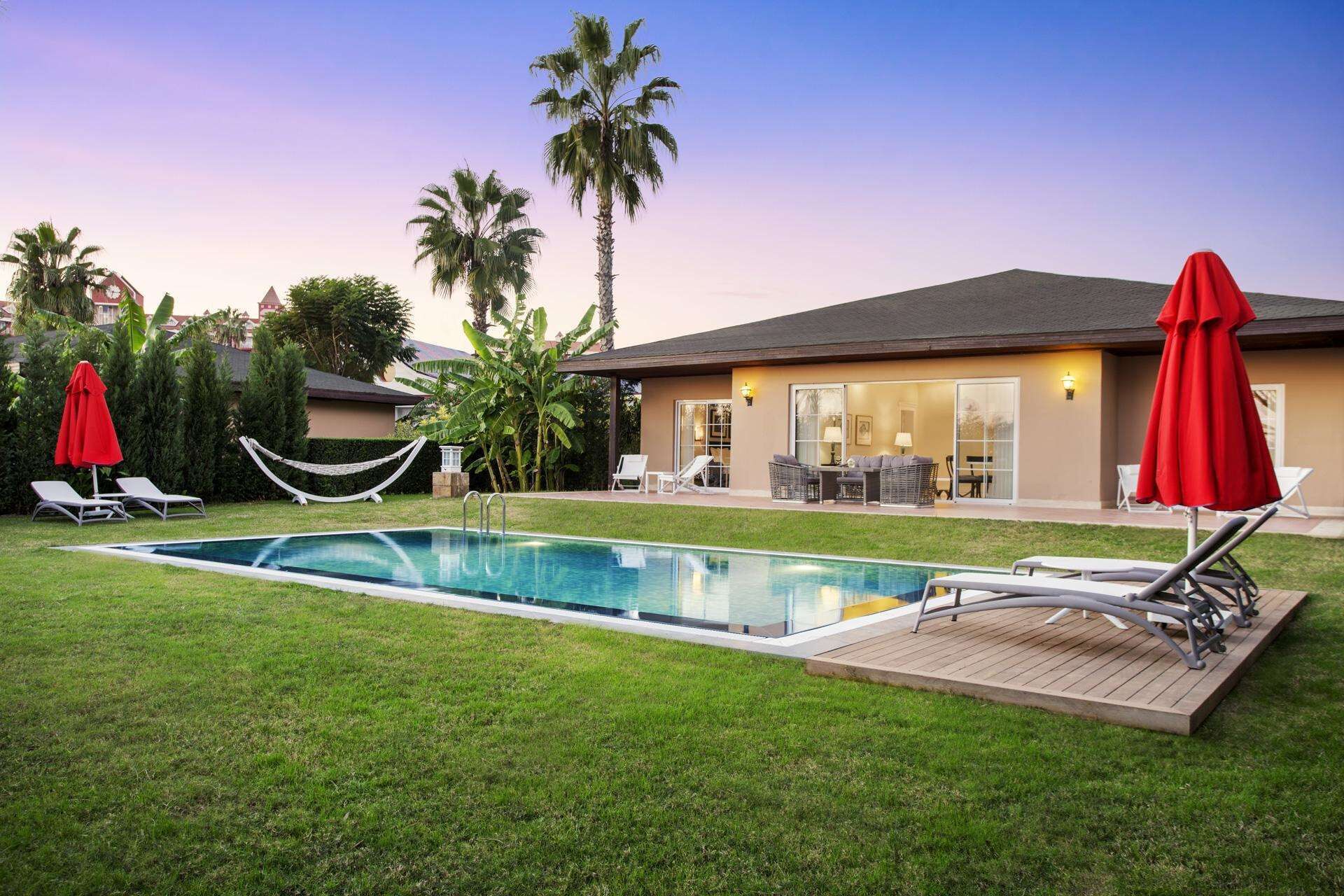 A swimming pool with lounge chairs and umbrellas, surrounded by a well-maintained lawn and palm trees.