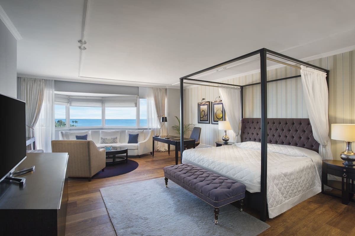 A four-poster bed with a canopy, a television, a desk, and a view of the sea.