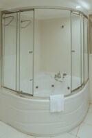 A modern bathroom with a glass-enclosed shower, a white bathtub, and a towel hanging on the tub.