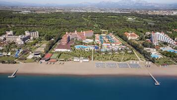 Vista aérea de un complejo turístico con varias edificaciones, un amplio área de piscina y una playa.
