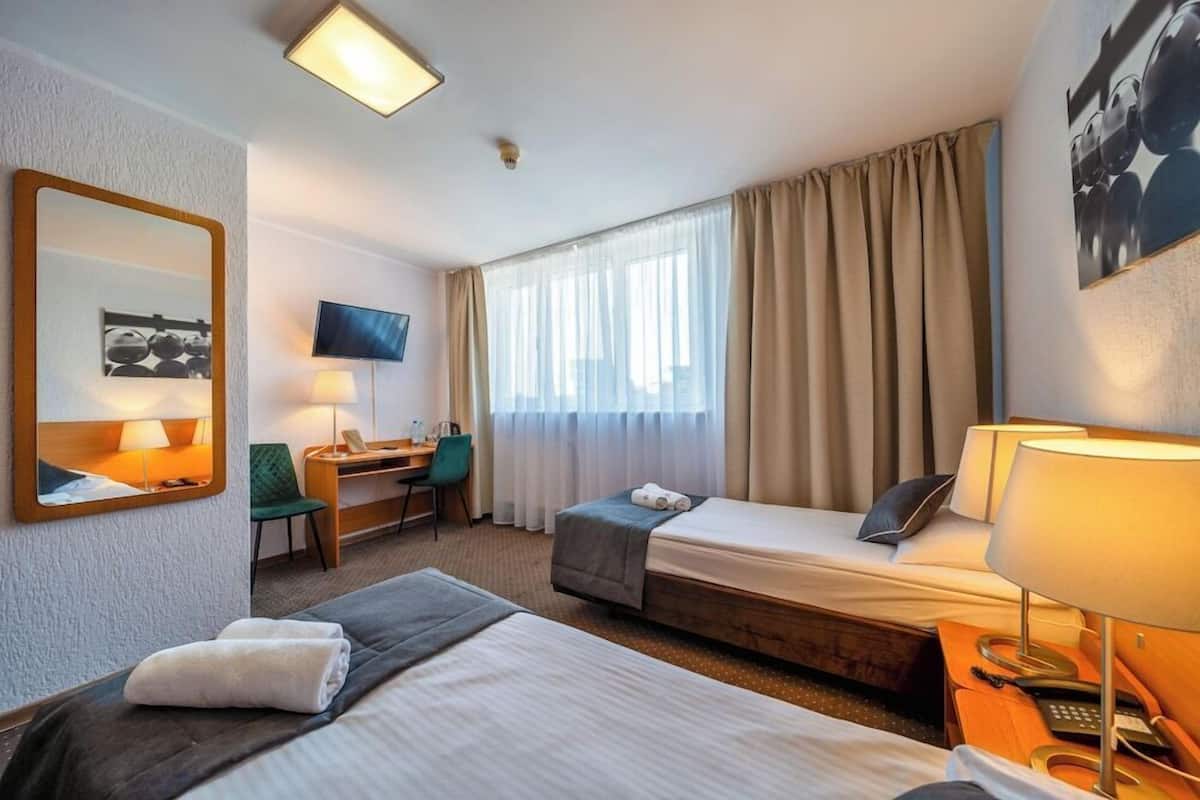 A hotel room with two beds, a desk, a chair, a TV, and a window with curtains.