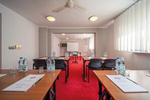 A conference room with a red carpet, wooden tables, and black chairs. There are water bottles on the tables, a whiteboard, and a ceiling fan. - Gromada (Poznan)