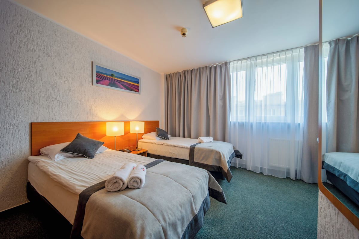 A hotel room with two beds, a painting on the wall, a window with curtains, and a headboard.