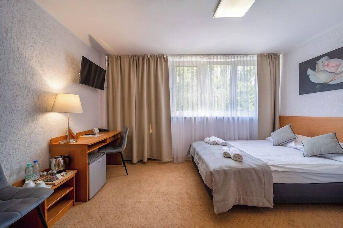 A hotel room with a bed, desk, chair, TV, and a window with curtains.