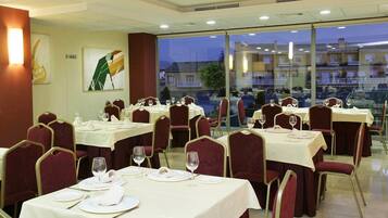Un restaurante con mesas dispuestas para comer, sillas y vistas a edificios a través de amplios ventanales.