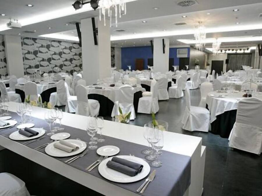Un salón de banquetes con mesas redondas dispuestas para un evento formal, con manteles blancos, cristalería y servilletas dobladas con cuidado.