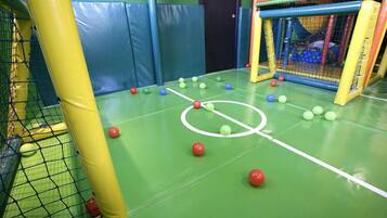 Ein Spielbereich im Innenbereich mit Fußballfeld, Spielgerüsten mit Netzen und gepolsterten Wänden.