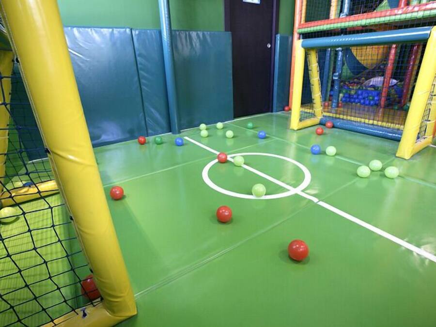 Un área de juegos interior con cancha de fútbol, estructuras de juego con red y paredes acolchadas.