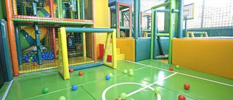 Un área de juegos interior con un arco de fútbol, red y varias pelotas.