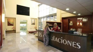 A reception desk with 'BS ULACIONES' signage, a large window, and a painting on the wall. - BS Capitulaciones (Santa Fe)