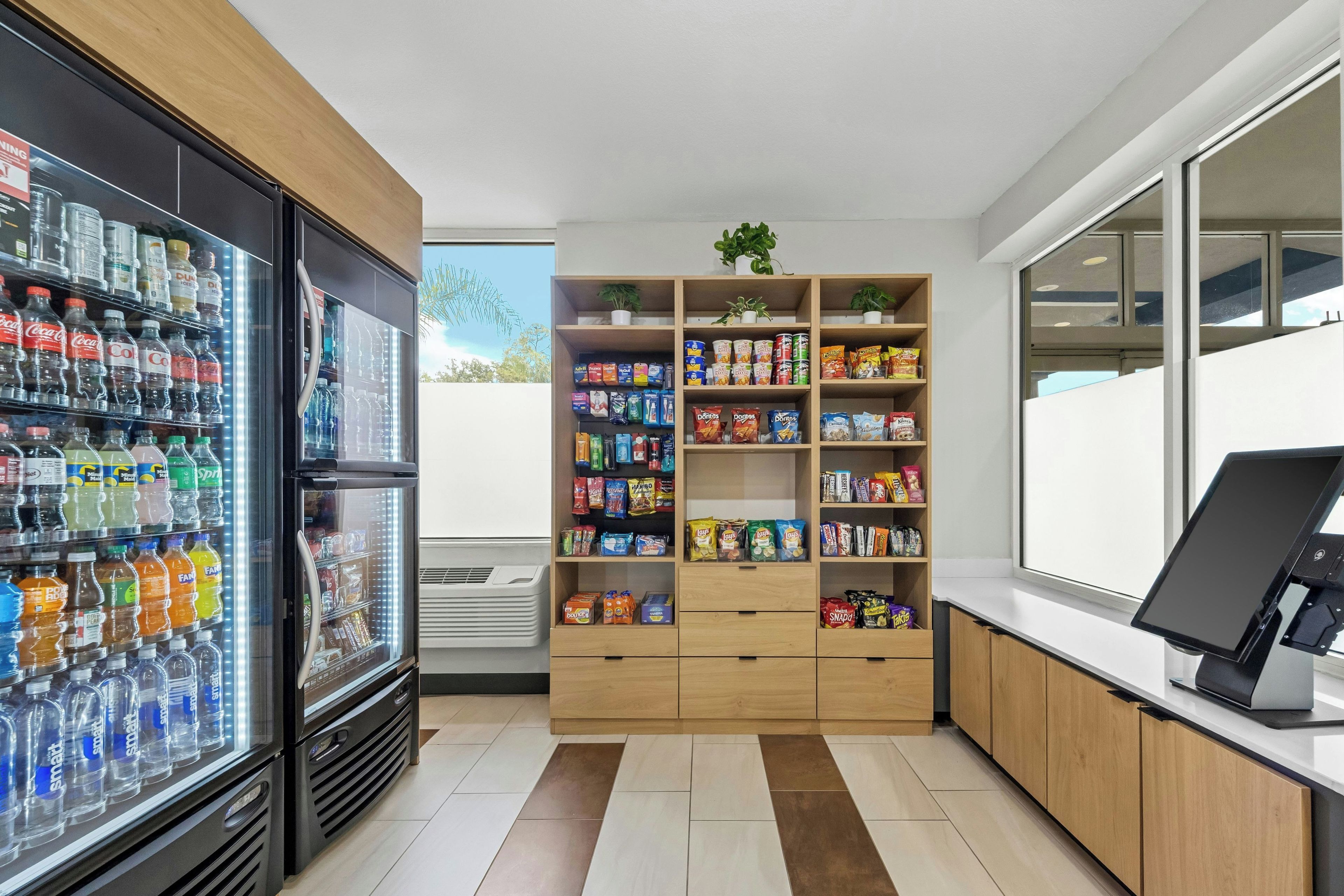Uma área de quiosques de autoatendimento com dispensador de bebidas refrigeradas, prateleiras com lanches e terminal de pagamento.